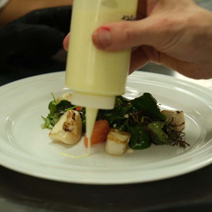 Scallops and greens dressed with a warm sauce at the pass