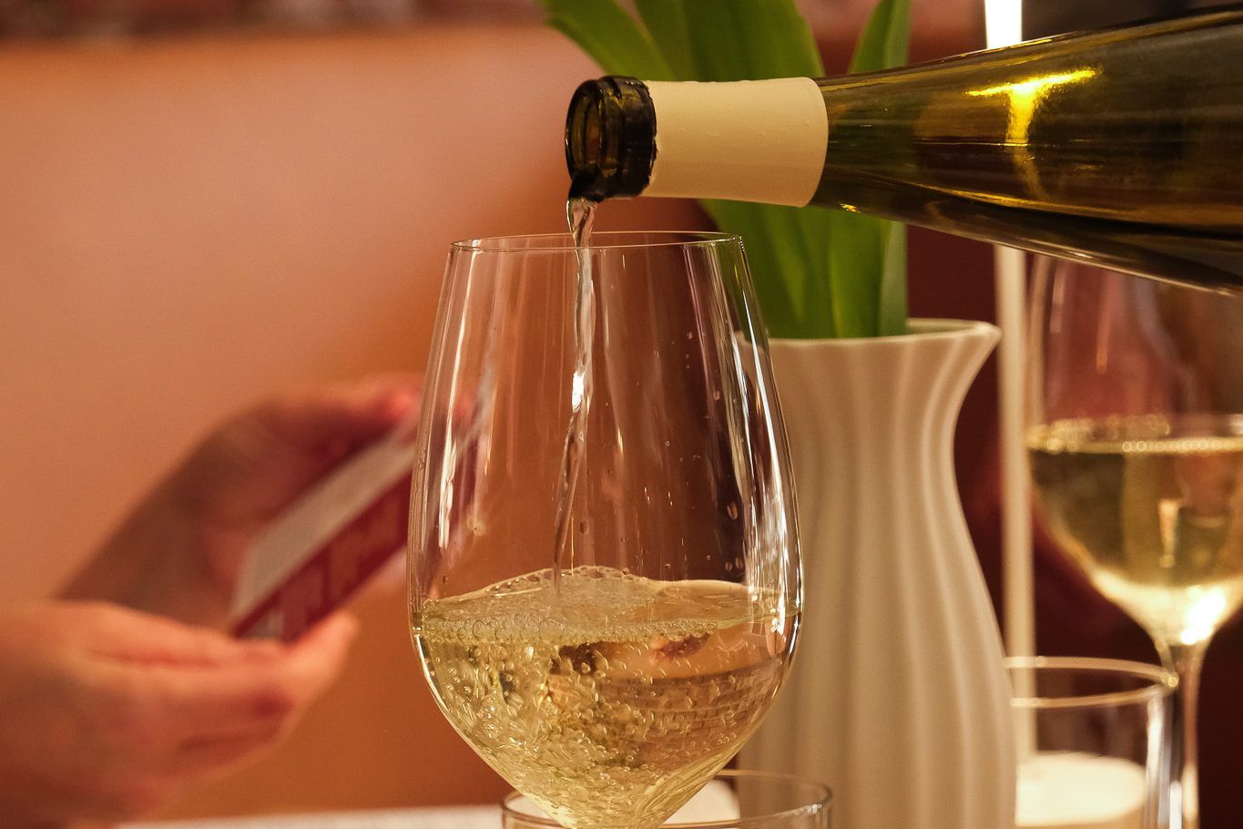 A glass of white wine and tulips on a set table against exposed brick at Clementina